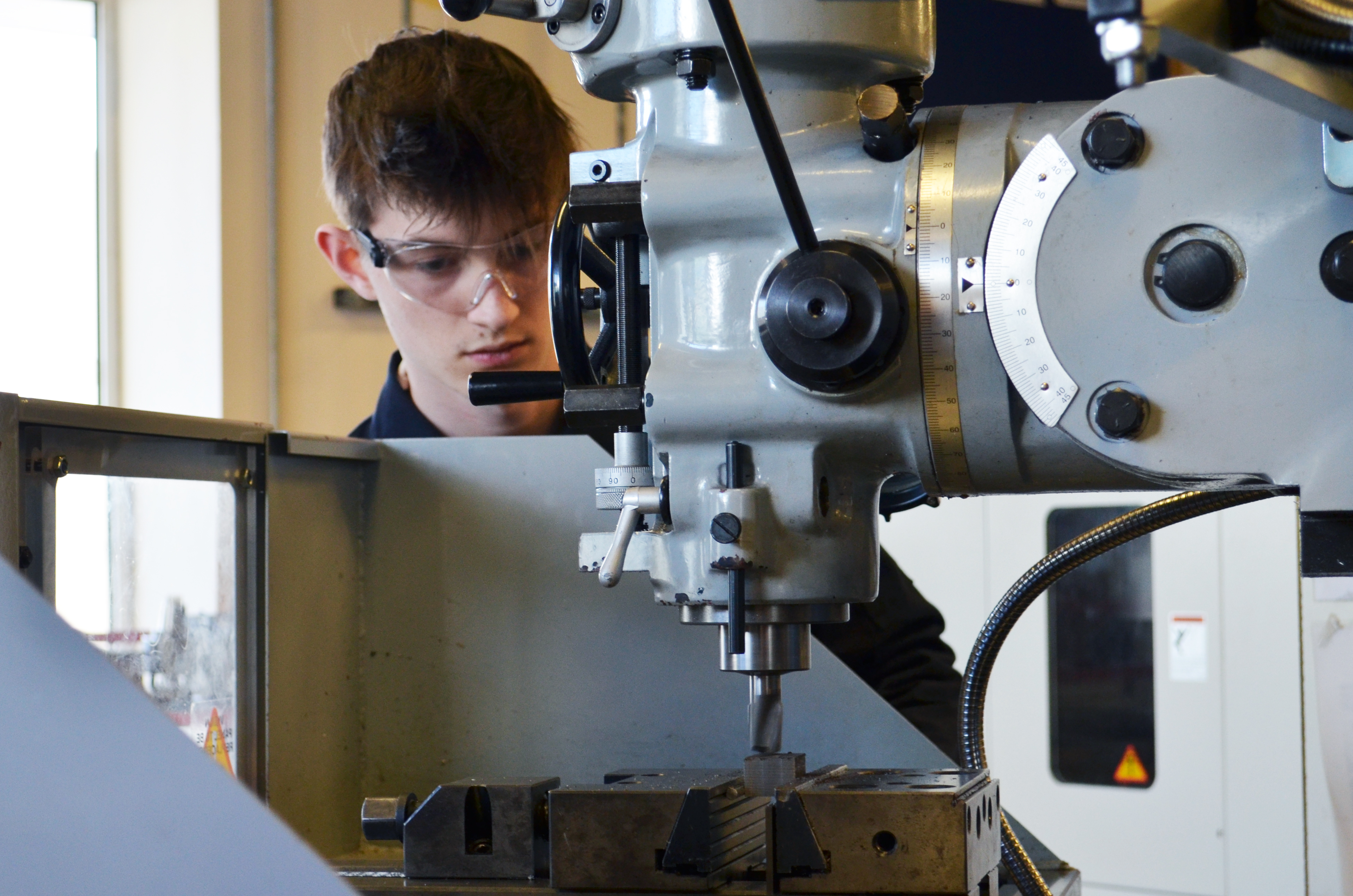 Student wearing safety goggles working at a machine in the Hi Tech & Digital Centre