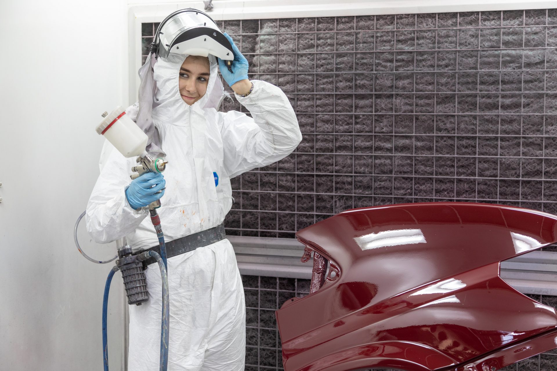 Vehicle bodywork student spraying and painting car bonnet.