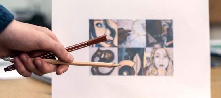 Pen and pencil being held in front of a picture.