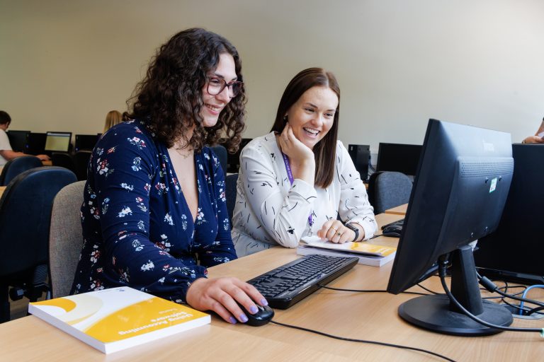 Accounting student working on computer in classroom with teacher smiling